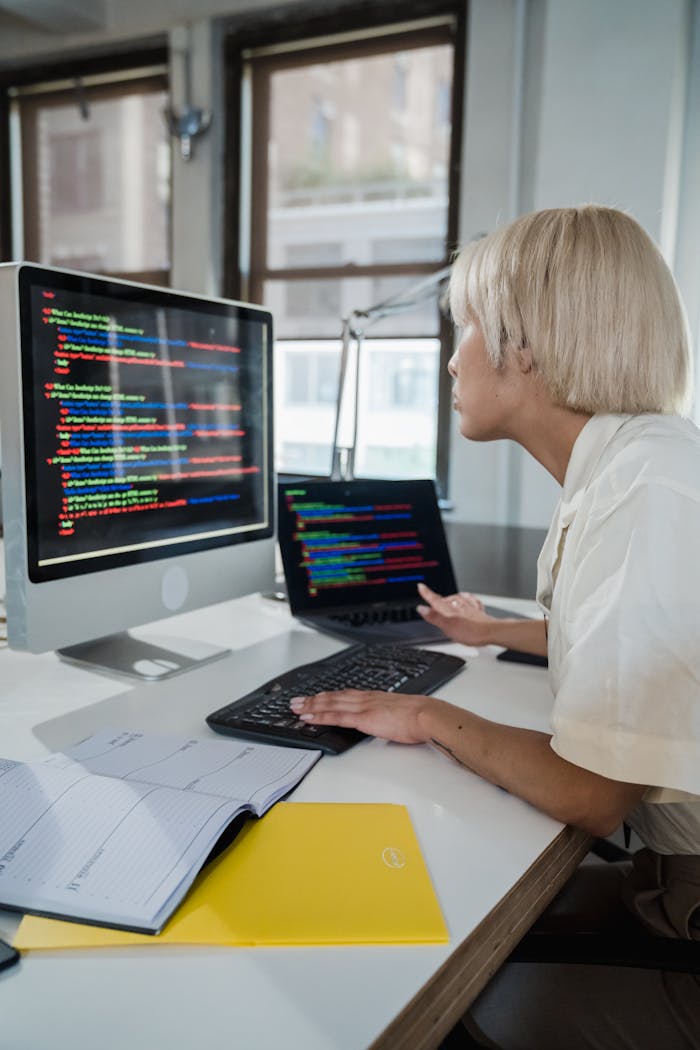 Services Woman with blonde hair programming on a computer in a modern office, focused on multicolored script on screen.