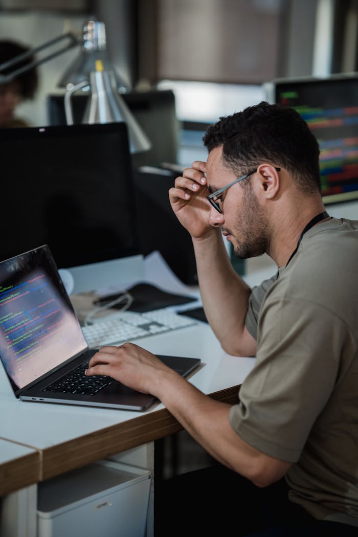 About A man intensely focused on coding at a desk in a modern office environment.