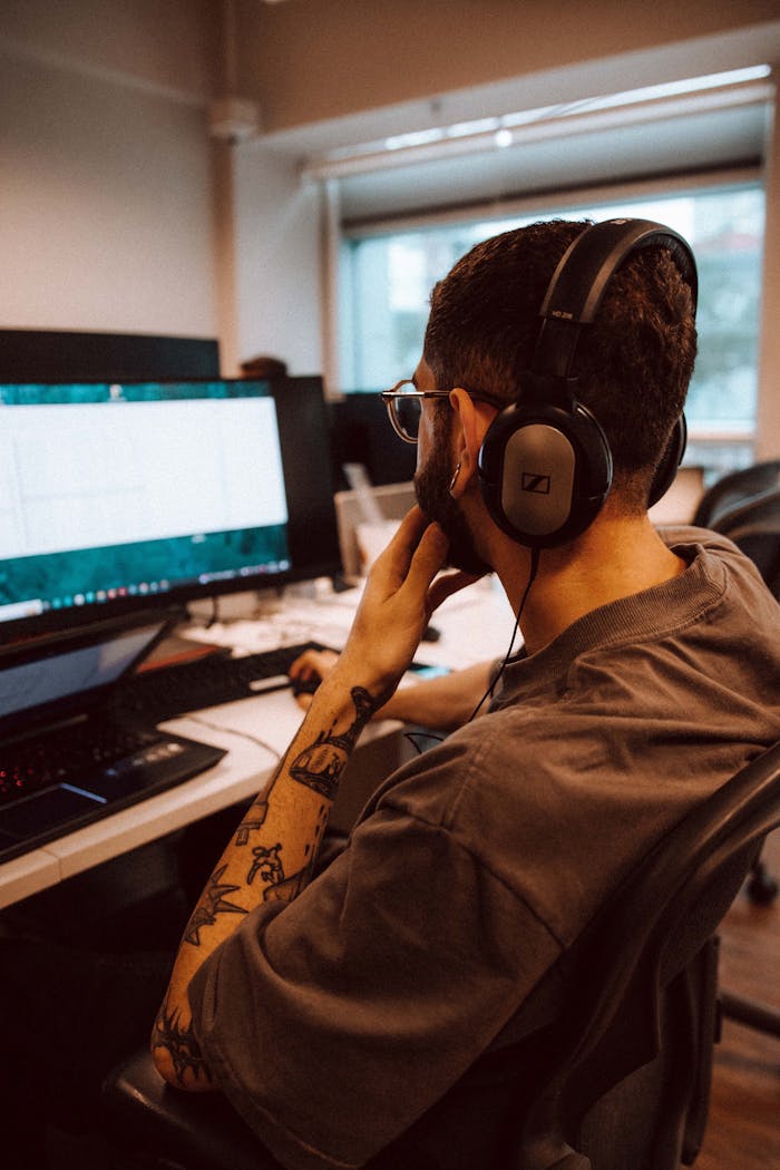 Services Young adult man focused on computer screen while wearing headphones in an office setting.