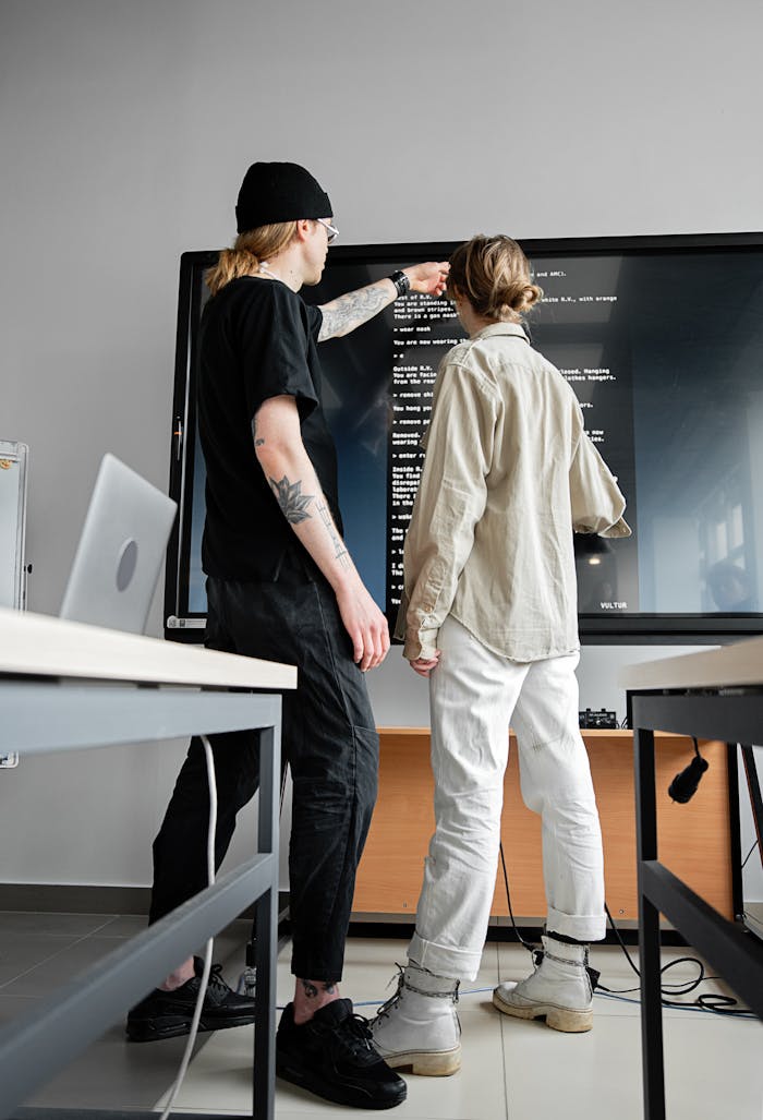 Services Two young adults collaborating on a coding project in a modern office setting.